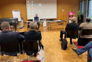 Das Foto zeigt die Tagung der Dekanatssynode im Herbst 2022, als es um das Thema Diakonie ging. Dekan Jochen Wilde sitzt am Tisch als Dr. Claudia Stadelmann-Laski vom Präsidium am Pult stehend die Synodalen zur Tagung begrüßt. 