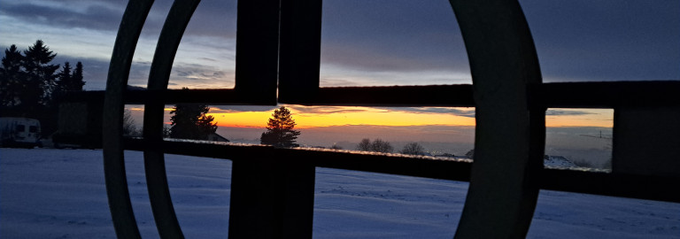 Kreuz vor Sonnenutergang in winterlicher Landschaft