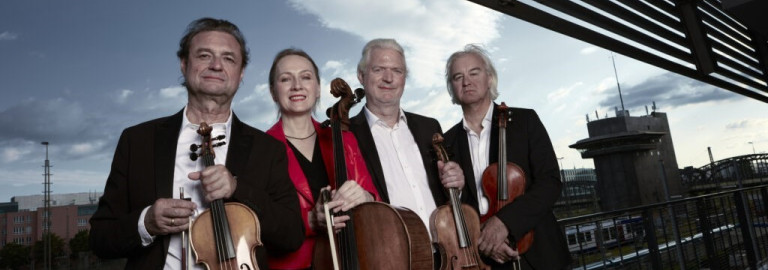 Die vier Musiker des Modern String Quartett stehen in Mitten moderner Architektur. Im Hintergrund ist der Himmel sichtbar.