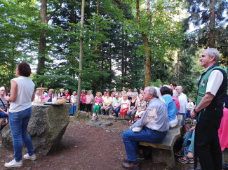 Viele Menschen sitzen auf den Bänken der Naturkapelle auf dem Geyersberg.