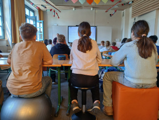 Schüler:innen von hinten auf ihren neuen "Stühlen" sitzend