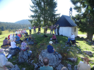 Gottesdeinstbesucher sitzen im Rund neben einer Bergkapelle