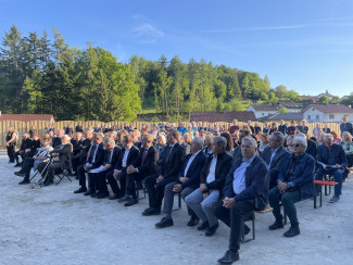 Besucher sitzen auf Bierbänken im Freien und hören der Lesung zu