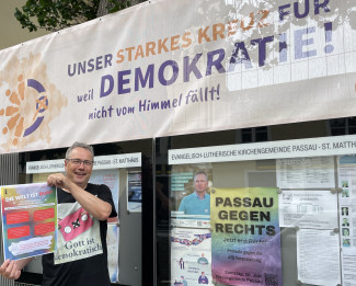 Dekan Wilde mit dem Plakat "Die Welt ist bunt" vor dem Schaukasten der Gemeinde St. Matthäus