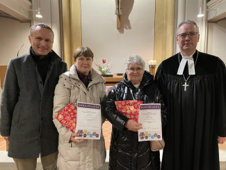Dekan Jochen Wilde und David Schäfer ehren Olga Schmidt und Nina Akubcik. Sie stehen vor dem Altar der Stadtpfarrkirche. Im Hintergrund sieht man das Kreuz.