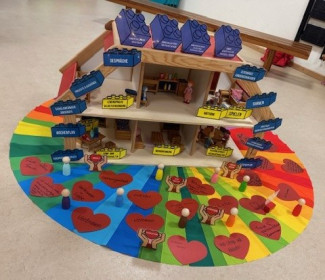 Ein Regenbogenkreis mit Haus und Legossteinen, die das Konzerpt des Kindergartens symbolisieren.