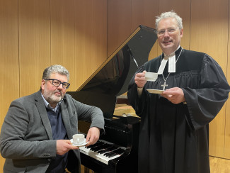 Ralf Albert Franz udn Dekan Jochen Wilde mit Kaffeetassen vor dem Flügel sitzend und stehend