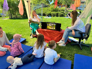 Kinder sitzen auf der Wiese und hören der Märchenerzählerin zu.