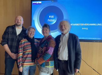 Die vier Mitarbeiterverteter:innen stehen vor einem rießigen Monitor zur Videoübertragung im Evangelishcen Zentrum.