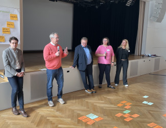 Zwischen den Moderatior:innen steht das Dekan:innen-Trio und steht Rede und Antwort