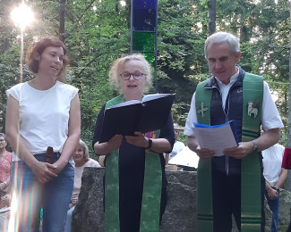 Verena Blab, Gabi Neumann-Beiler und Magnus König stehen vor dem Altar der Naturkapelle am Geyersberg und singen. Im Hinergrund ist das Gipfelkreuz zusehen.