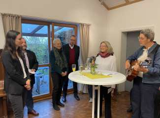 Im Gemeindesaal hört Pfarrerin Popp das niederbayerische Lied gesungen von Frau Weihe und Tischer an der Gitarrew.