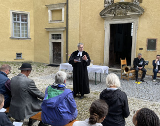 Dekan Wilde predigt im Innenhof von Schloss Neuburg und die Gemeinde sitzend auf Bierbänken hört zu.