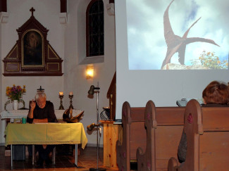 Der Autor liest in der Kirche. Rechts die Leinwand mit den Fotografien.