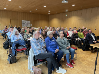 Die Synodalen sitzen im Evangelischen Zentrum Passau auf Stühlen und hören der Referentin zu
