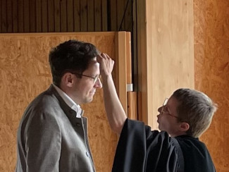 Annalena Hardinge malt bei der Tauferinnung ein Kreuz auf die Stirn von Dr. Philipp Augustin.