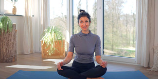 Eine Frau sitzt im Schneidersitz auf einer Yogamatte.